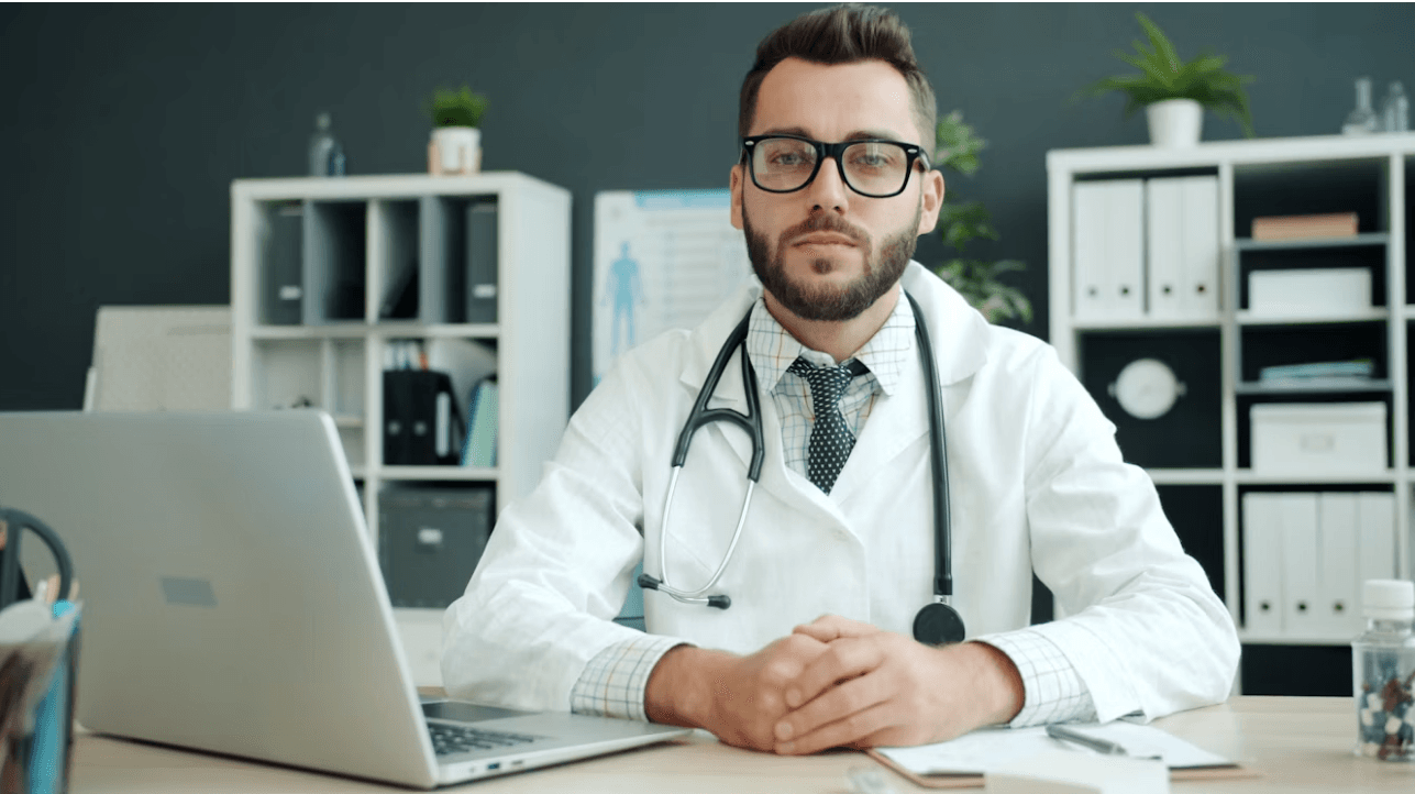 A doctor sitting at a desk with a laptop in a medical office.