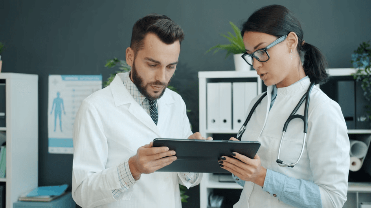 Two clinicians using a tablet in a medical office, representing healthcare IT support.