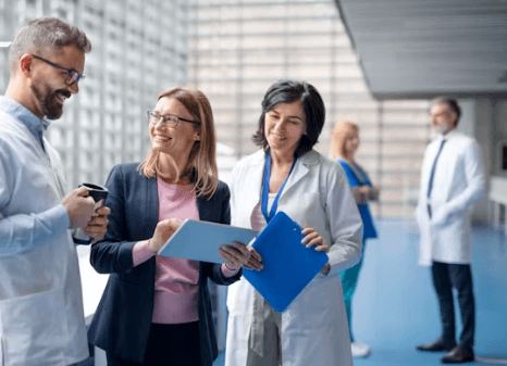 A healthcare team in white coats and scrubs reviewing patient information on a clipboard.