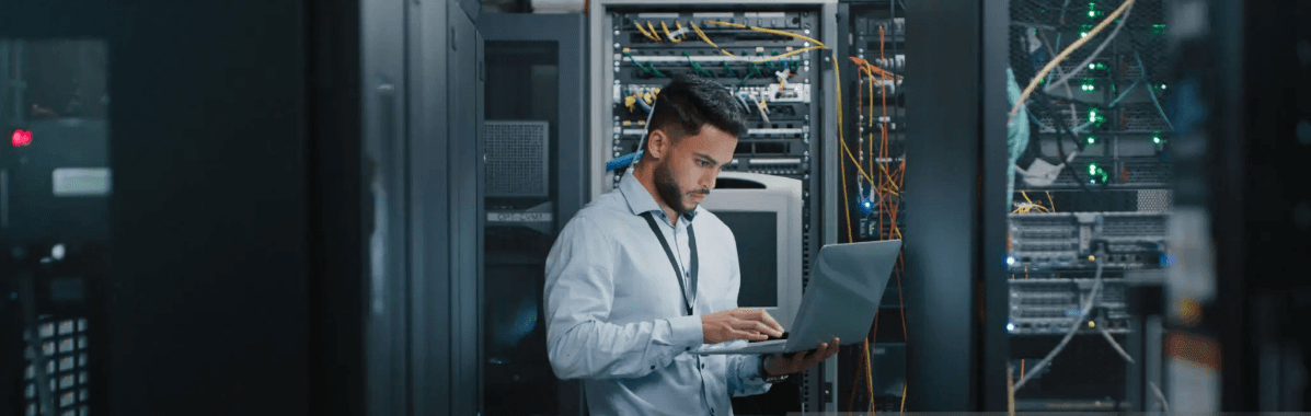An IT professional working on a laptop in a modern data center server room.