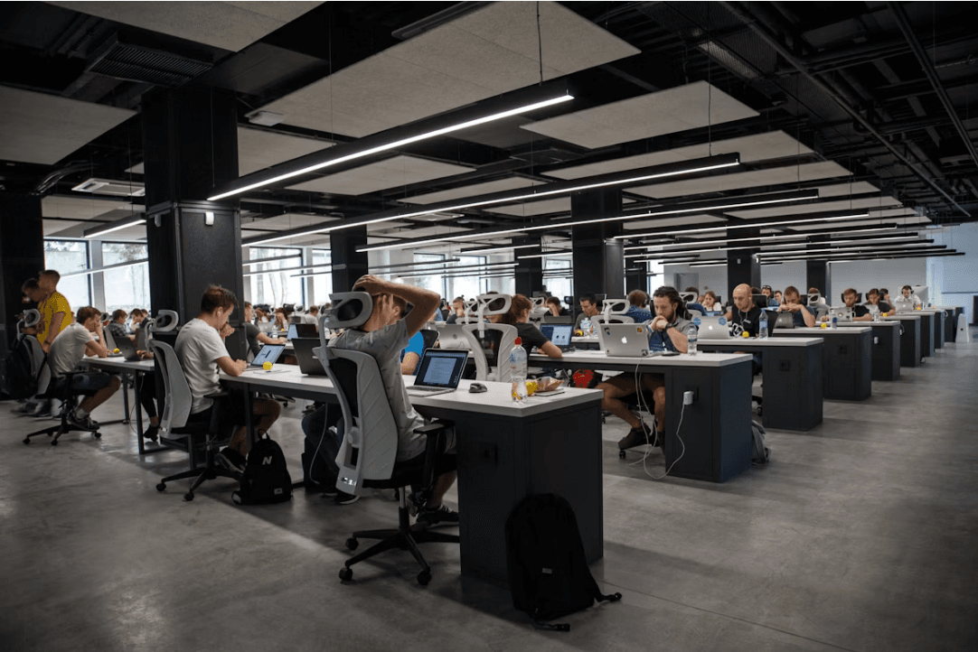 A busy open-plan technology office with staff working at rows of laptops.
