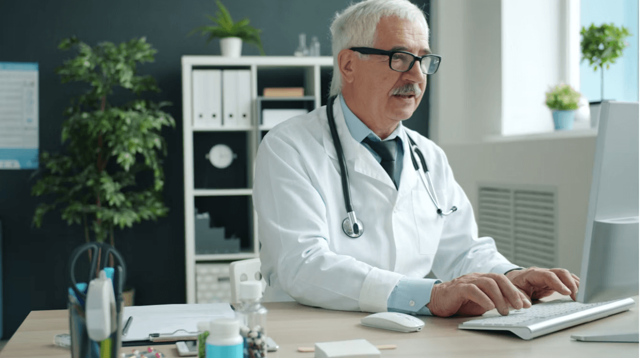 A doctor entering patient information at a desktop computer in a medical office.