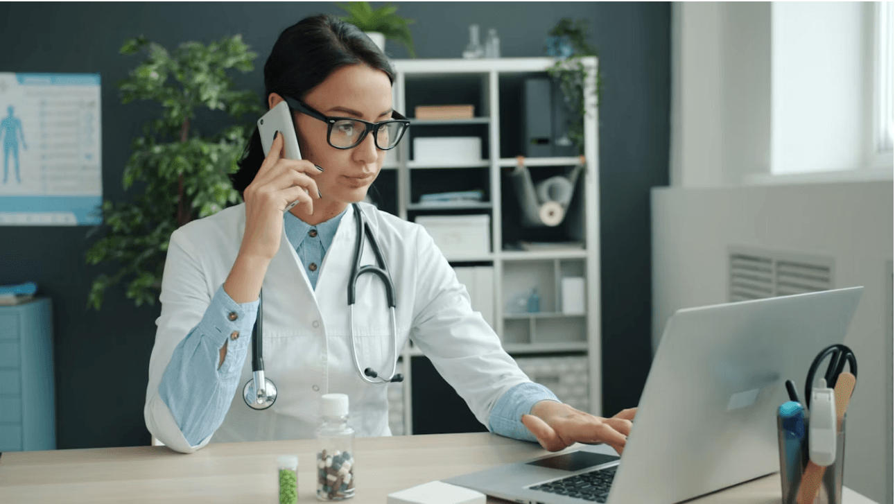 A healthcare professional on the phone at a laptop in a medical office.