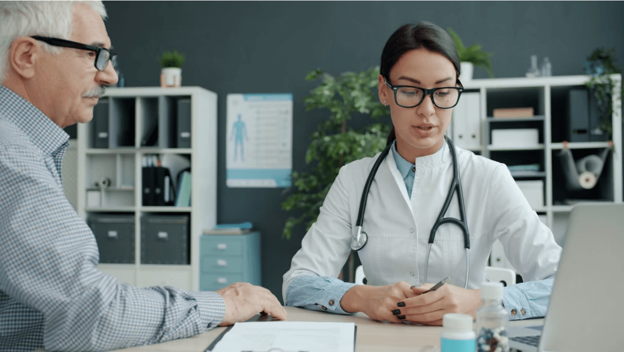 A doctor reviewing paperwork with a patient at a desk in a clinic.