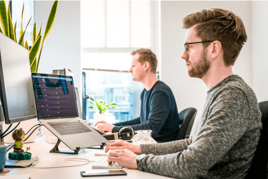 Software developers writing code at a dual-monitor workstation.